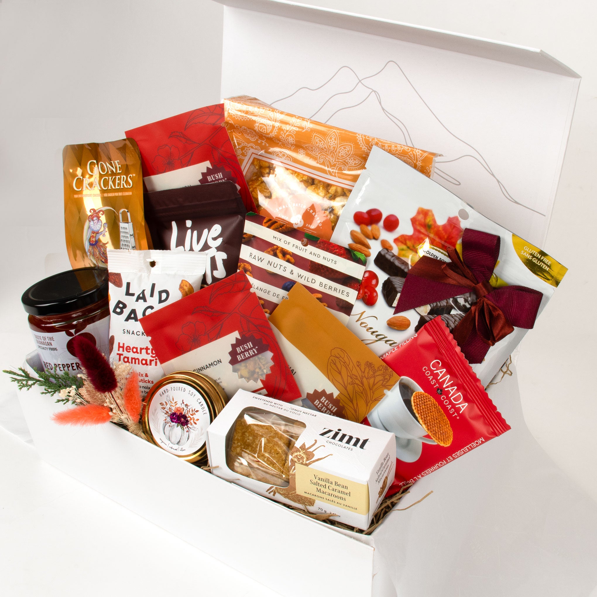 Assorted food items including cookies, jams, and packaged goods in a box on a white background