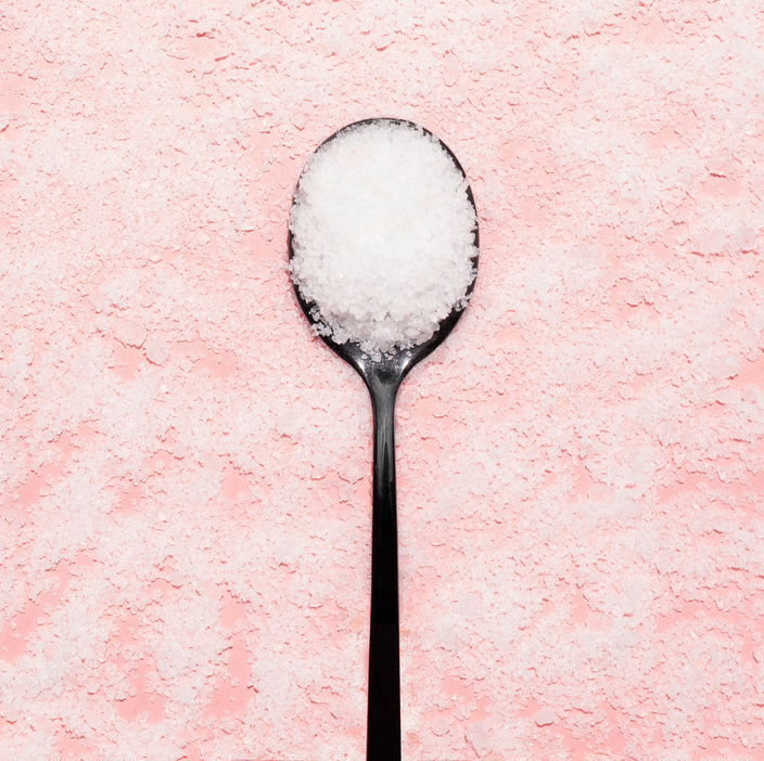 Black spoon filled with white sugar on a pink sugar background
