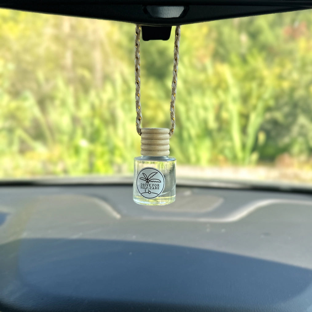 Car air freshener hanging from a car's rearview mirror with a blurred green outdoor background.