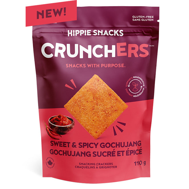 A stand-up pouch of Hippie Snacks Crunchers Sweet & Spicy Gochujang snack crackers, featuring a deep magenta and red design with a central image of a square golden-orange cracker and a small bowl of red sauce.