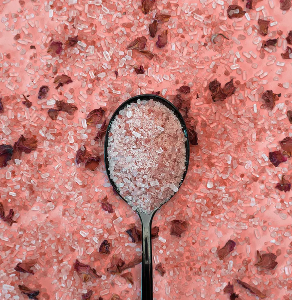 Spoon filled with pink salt crystals on a pink salt background