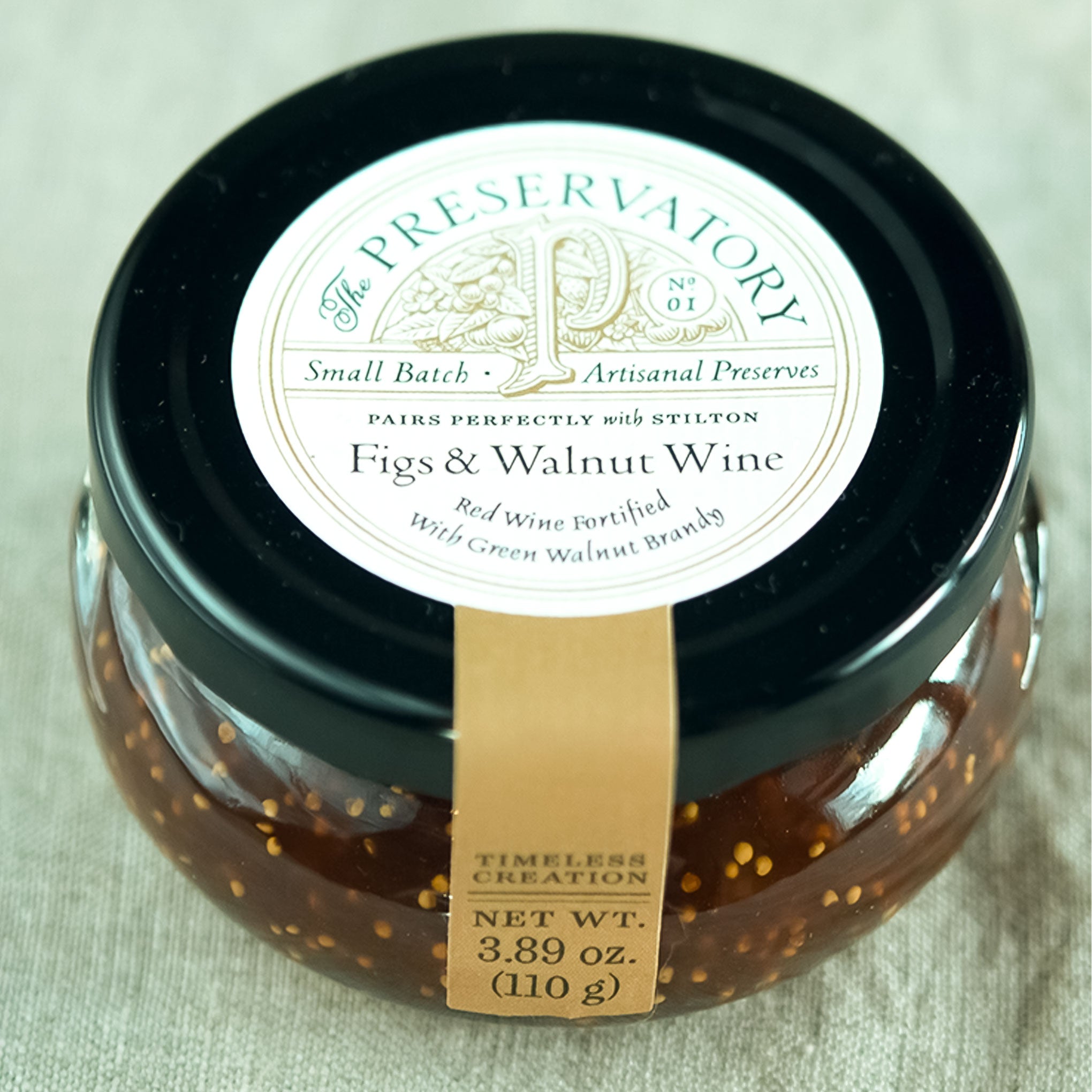 Jar of 'Figs & Walnut Wine' preserve with 'The Preservatory' label on a light background