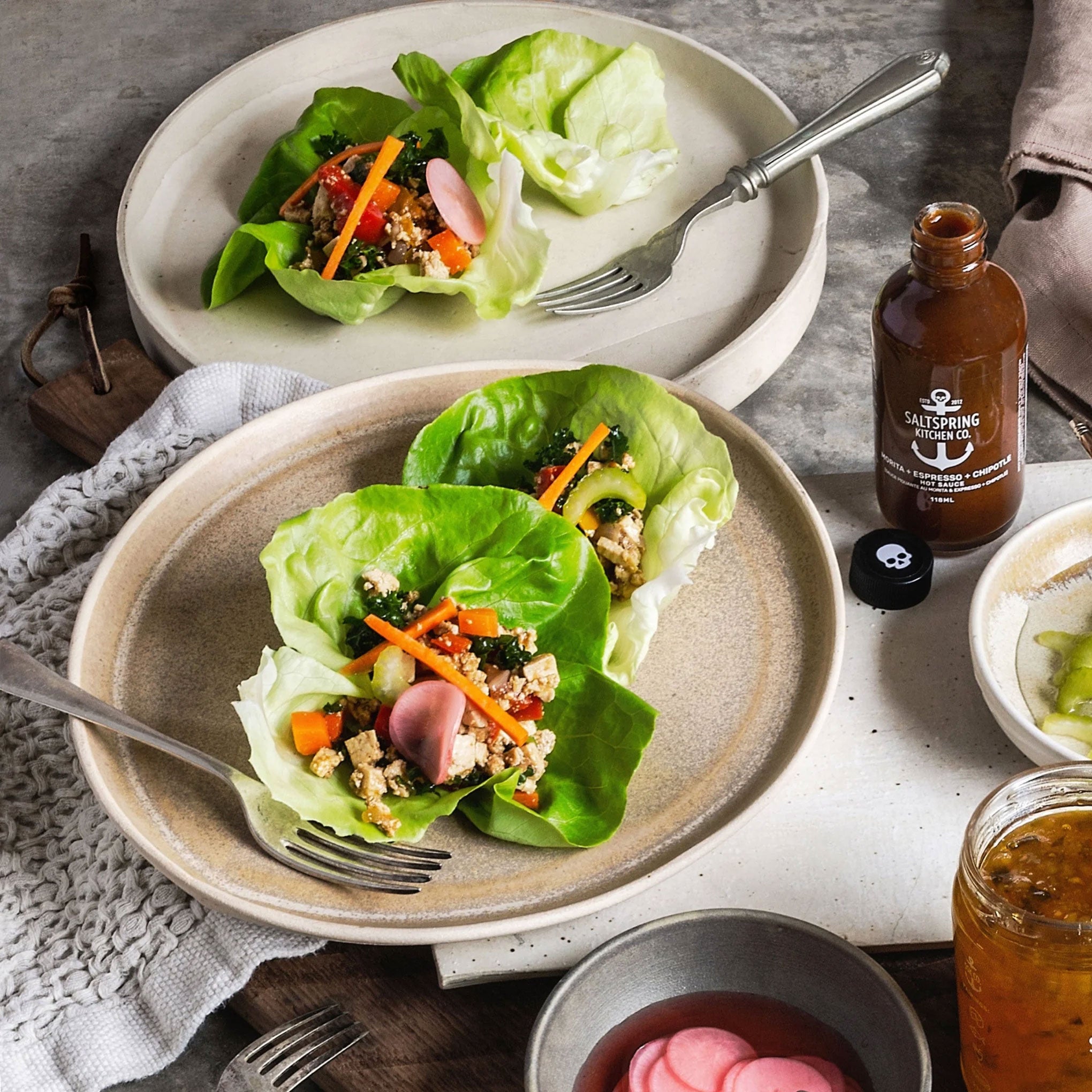 Two plates of lettuce wraps with a bottle of sauce on a table.