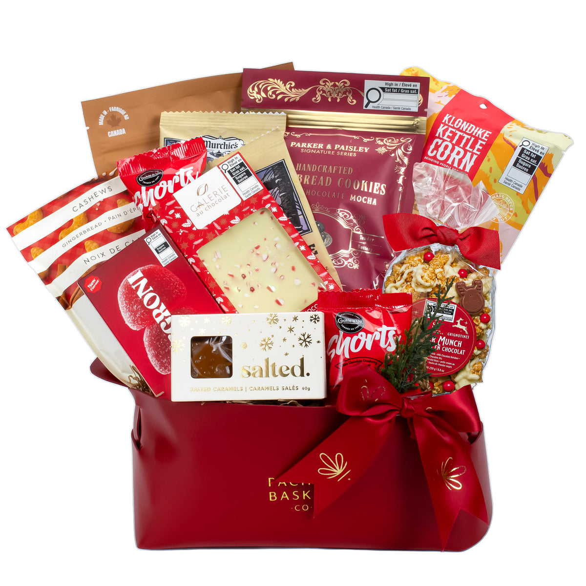 A red gift basket filled with assorted packaged snacks and treats, including Morris Salted Chocolate Bar, Parker & Priest Handmade Bread Cookies, Clonoke Kettle Corn, and a bag of mixed nuts, tied with a red ribbon on a white background.