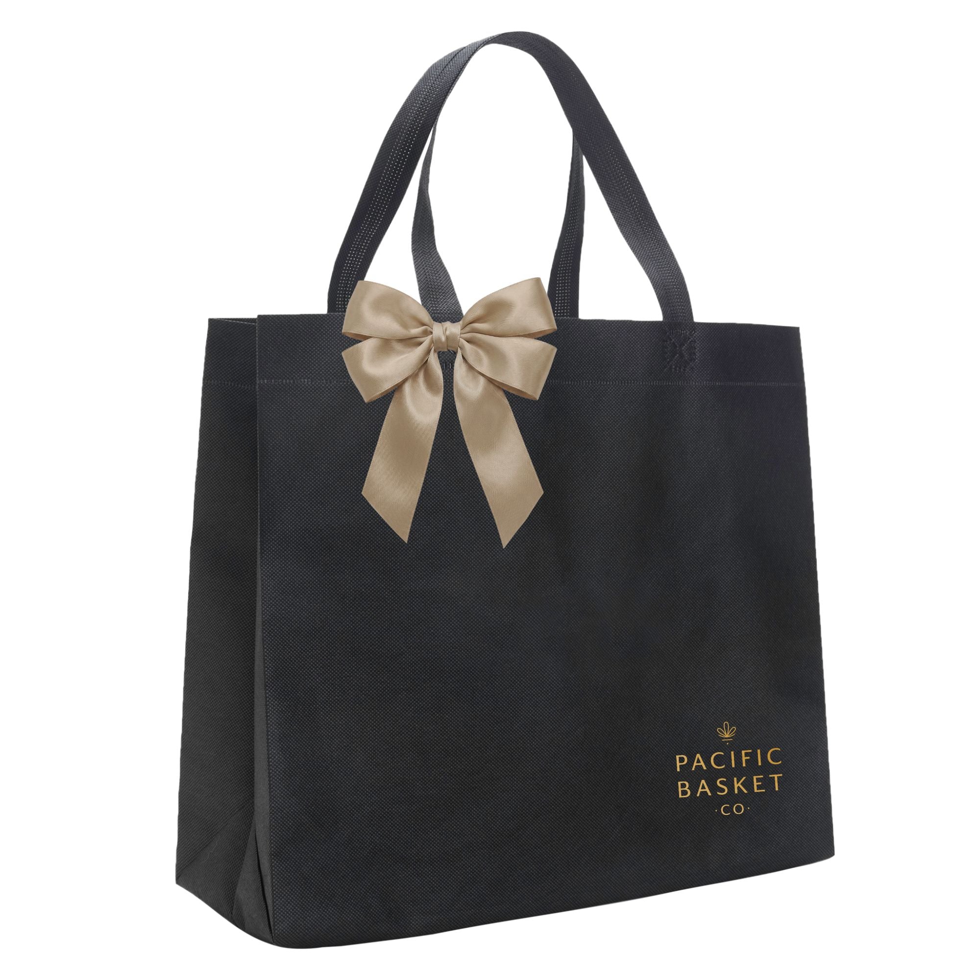 A black reusable tote bag with dual handles, a large beige satin bow at the top, and gold 'Pacific Basket Co' branding printed near the bottom right, shown on a plain white background.