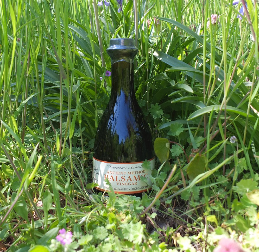 Bottle of balsamic vinegar surrounded by green grass and wildflowers