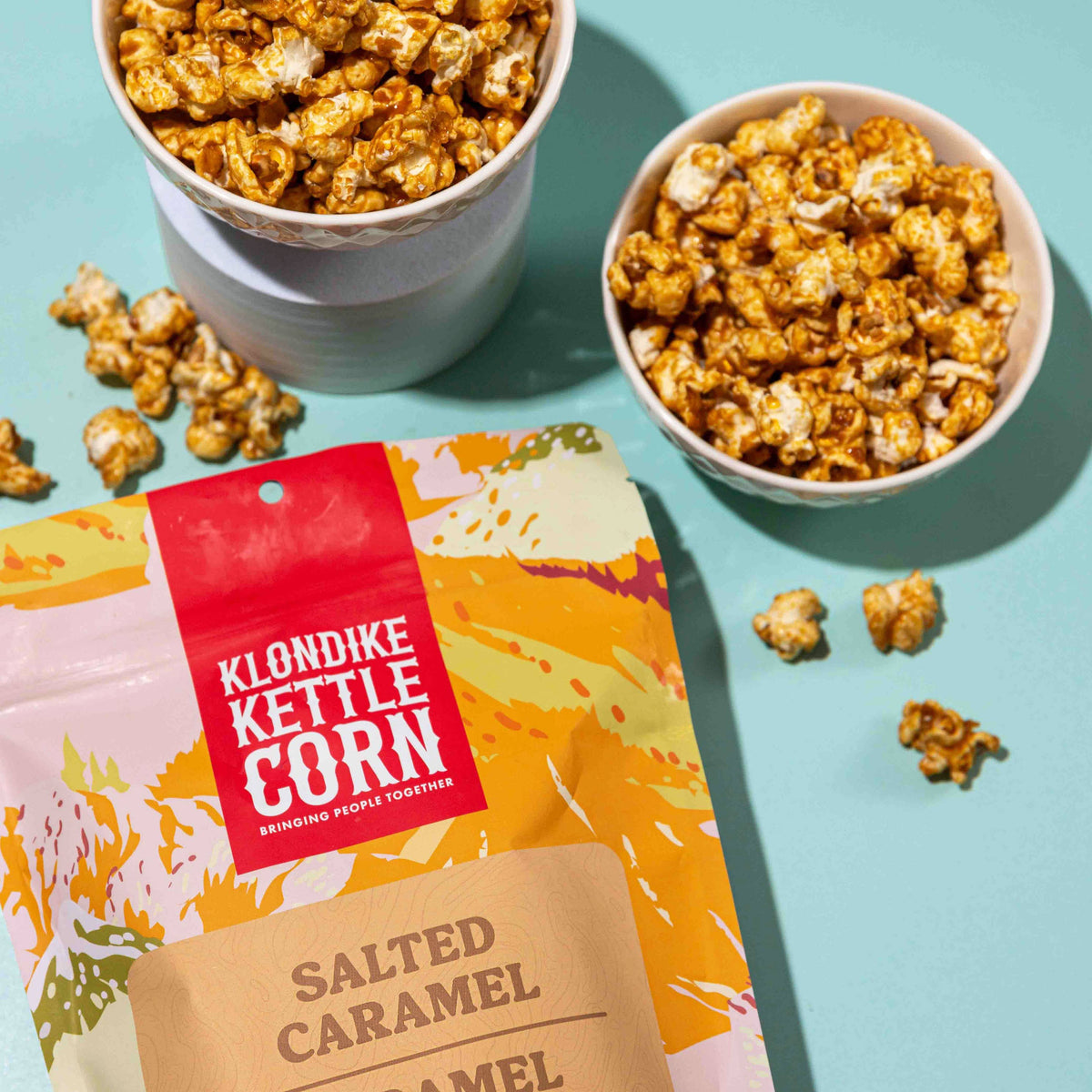 Klondike Kettle Corn salted caramel popcorn packaging with two bowls of popcorn on a light blue background.