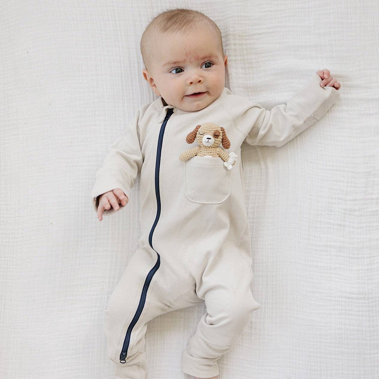 Baby wearing a beige onesie with a teddy bear design on a white textured surface