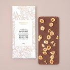 Chocolate bar with toasted hazelnuts and packaging on a beige background