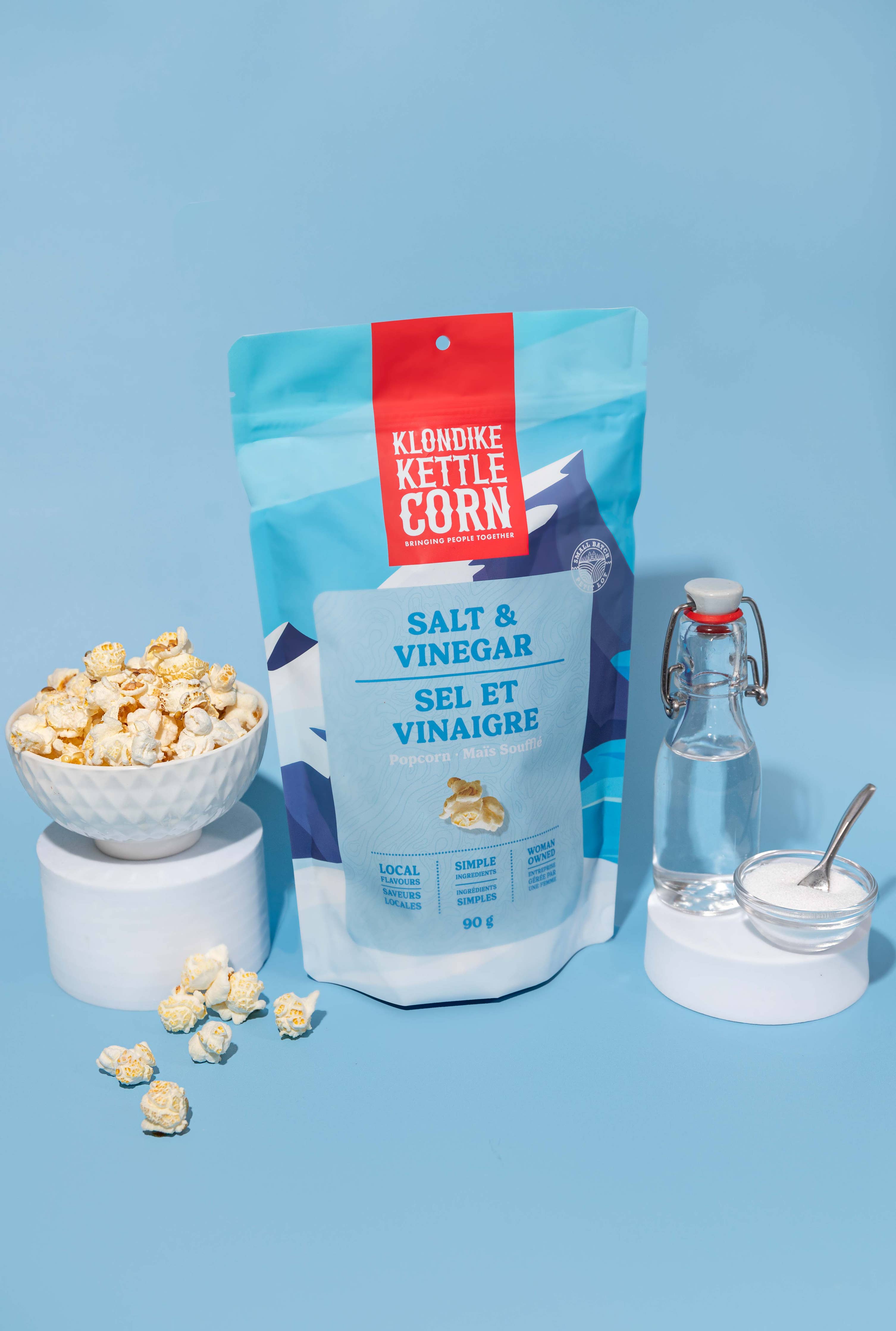 Klondike Kettle Corn salt and vinegar flavor packaging with popcorn and seasonings on a blue background