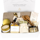 Open white Artisan Living gift box, beautifully arranged with a beige cotton throw, gold tin candle, Rousseau chocolate bar, ceramic mug with ribbon, and Drizzle honey jar.