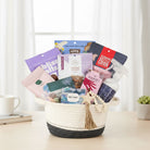 Basket filled with tea, snacks, bath salt, soap and a room spray bottle