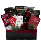 A Christmas-themed gourmet gift hamper in a black box, filled with assorted snacks and treats including Terroir dark chocolate bar, Red Wine, Gone Crackers, and  Shortbread Cookies, decorated with green pine branches and a red bow.