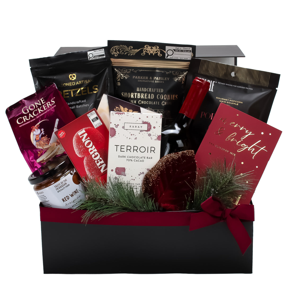A Christmas-themed gourmet gift hamper in a black box, filled with assorted snacks and treats including Terroir dark chocolate bar, Red Wine, Gone Crackers, and  Shortbread Cookies, decorated with green pine branches and a red bow.