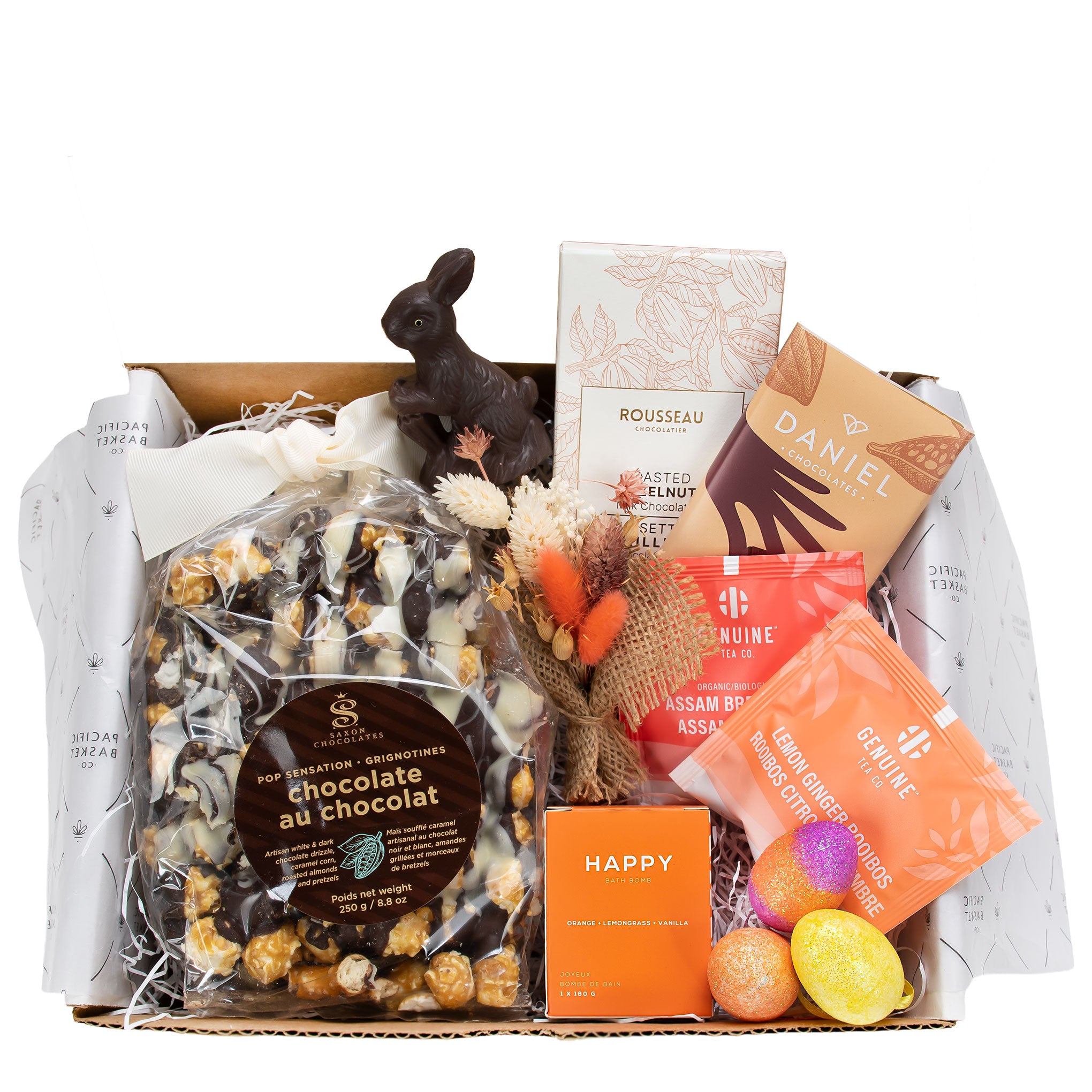 Easter gift box featuring chocolate popcorn, two chocolate bars, orange-toned artisan tea, and a Happy bath bomb in a mailer box.