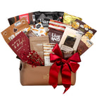A chocolate and snack gift basket filled with assorted packaged chocolates, nuts, and treats, tied with a large red ribbon and decorated with red berries, on a white background.