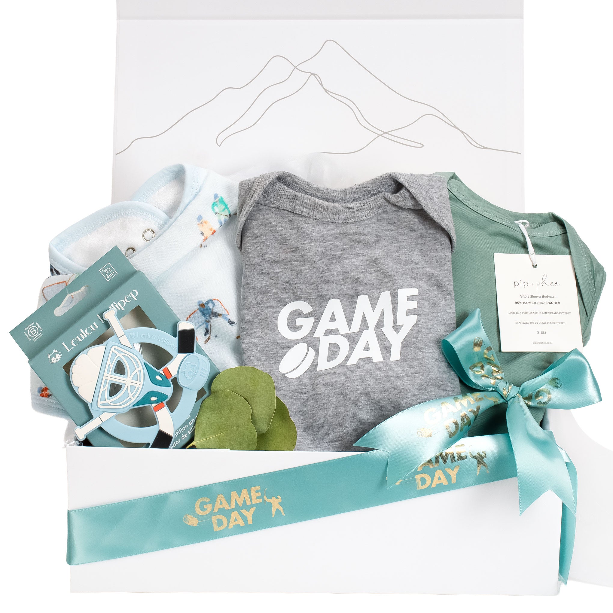 Game Day hockey baby gift box featuring a grey heathered bodysuit, sage green Pip and Phee bamboo onesie, Loulou Lollipop hockey bib, and a blue silicone mask teether in a white box with mountain line art.