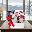 Gift basket with snacks and drinks on a table in a room with large windows showing a snowy landscape.