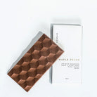 Bar of KARAT Maple Pecan chocolate with a textured, dimpled surface, shown next to its white packaging box on a clean white background
