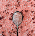 Spoon filled with pink salt crystals on a pink salt background