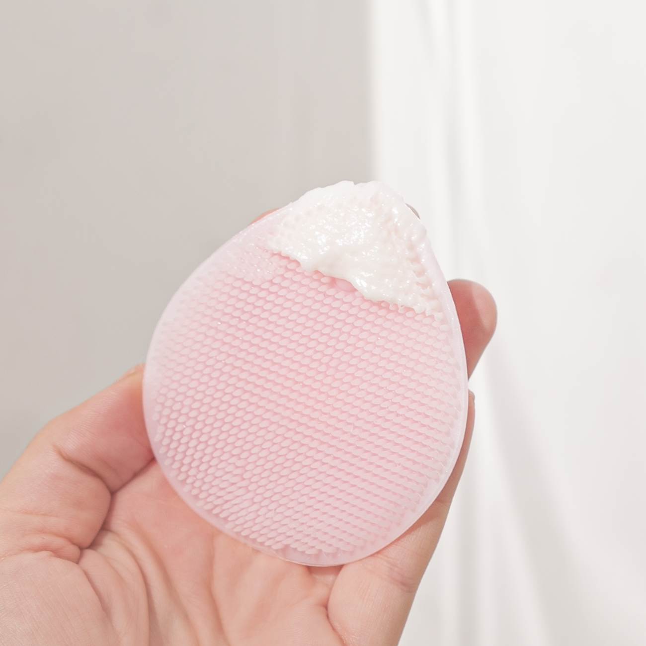 Pink silicone sponge held in a hand against a neutral background