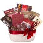 A festive holiday gift basket filled with assorted packaged snacks and treats, tied with a wide red ribbon and bow. Visible items include a red card reading 'merry & bright,' a bag labeled 'Kloninke Kettle,' a brown package labeled 'Rousseau,' and other holiday-themed packaged goods on a plain white background.