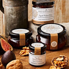 Jars of 'The Preservatory' Figs & Walnut Wine on a wooden surface with figs and walnuts.
