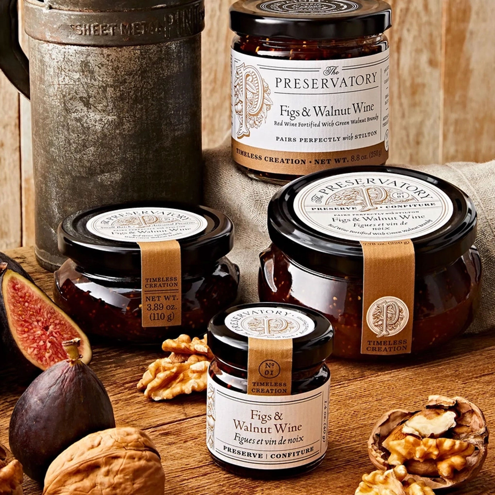 Jars of 'The Preservatory' Figs & Walnut Wine on a wooden surface with figs and walnuts.