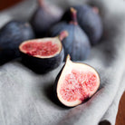 Figs on a gray cloth with one cut open to reveal pink flesh.