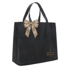 A black reusable tote bag with dual handles, a large beige satin bow at the top, and gold 'Pacific Basket Co' branding printed near the bottom right, shown on a plain white background.