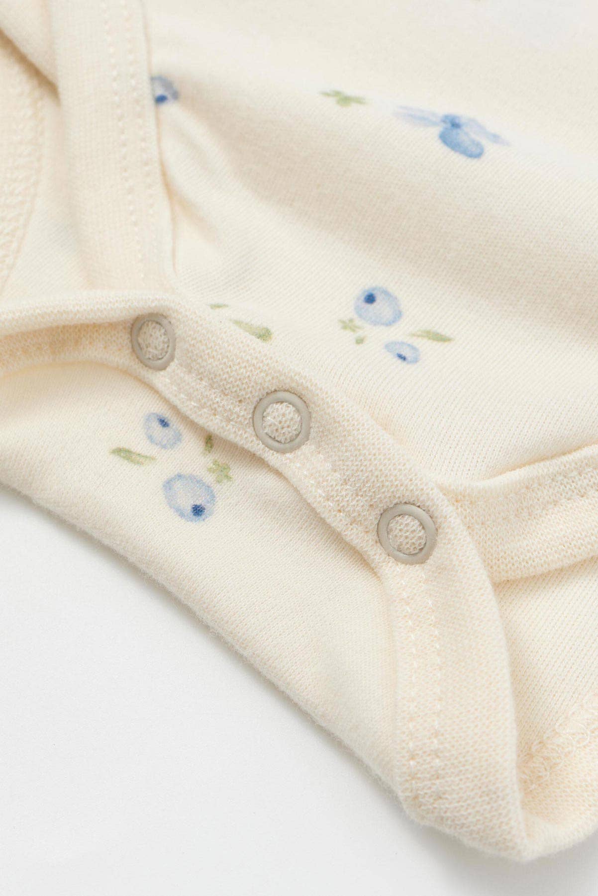 Close-up of a cream-colored baby outfit with floral embroidery on a white background